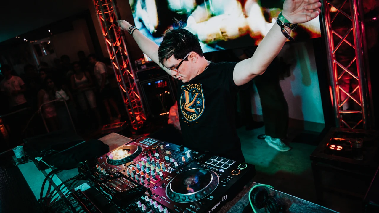 Víctor Zurano levantando los brazos durante una sesión de DJ techno en una cabina con luces de escenario