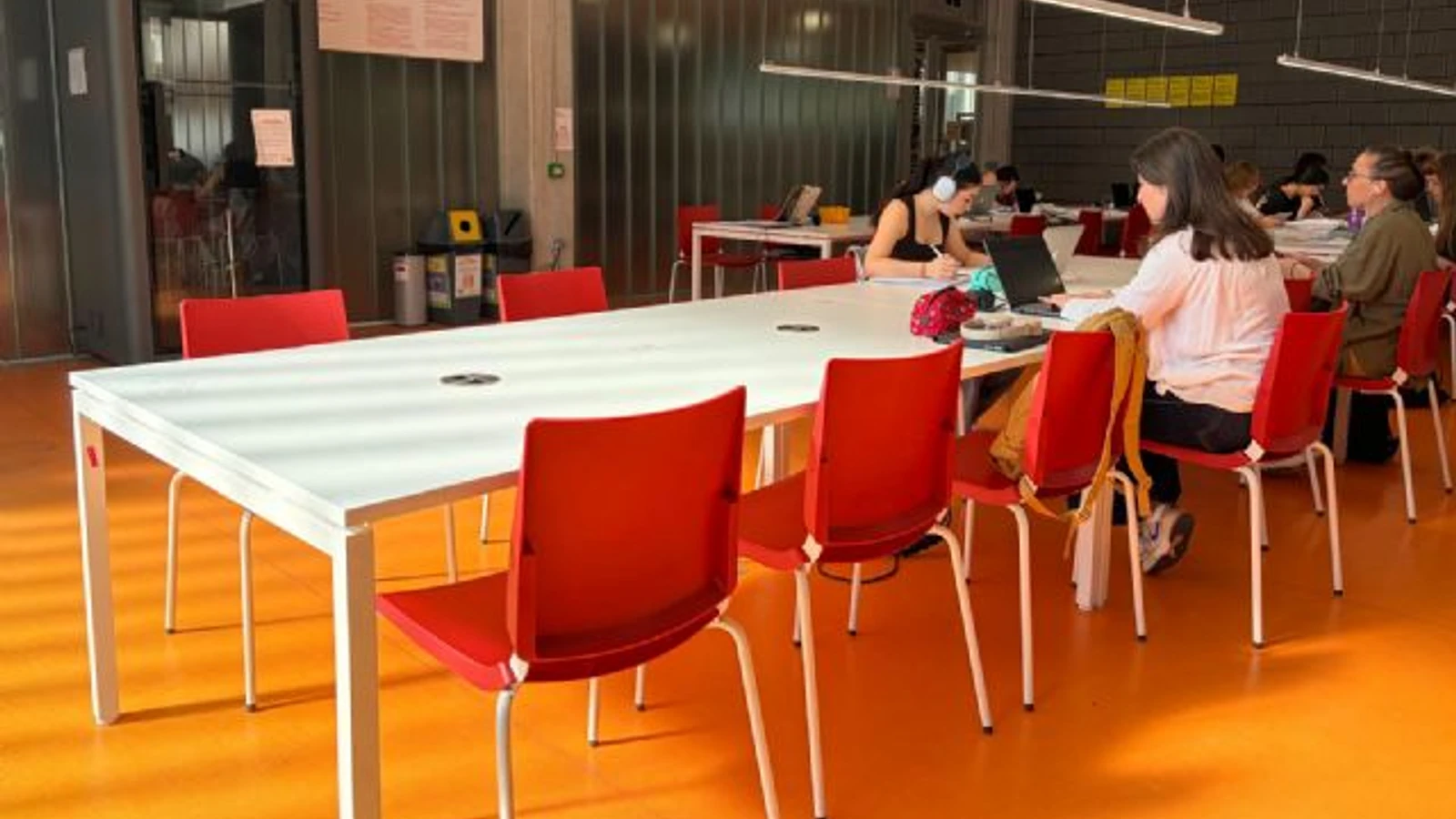 Personas estudian en una sala municipal equipada con mesas y sillas