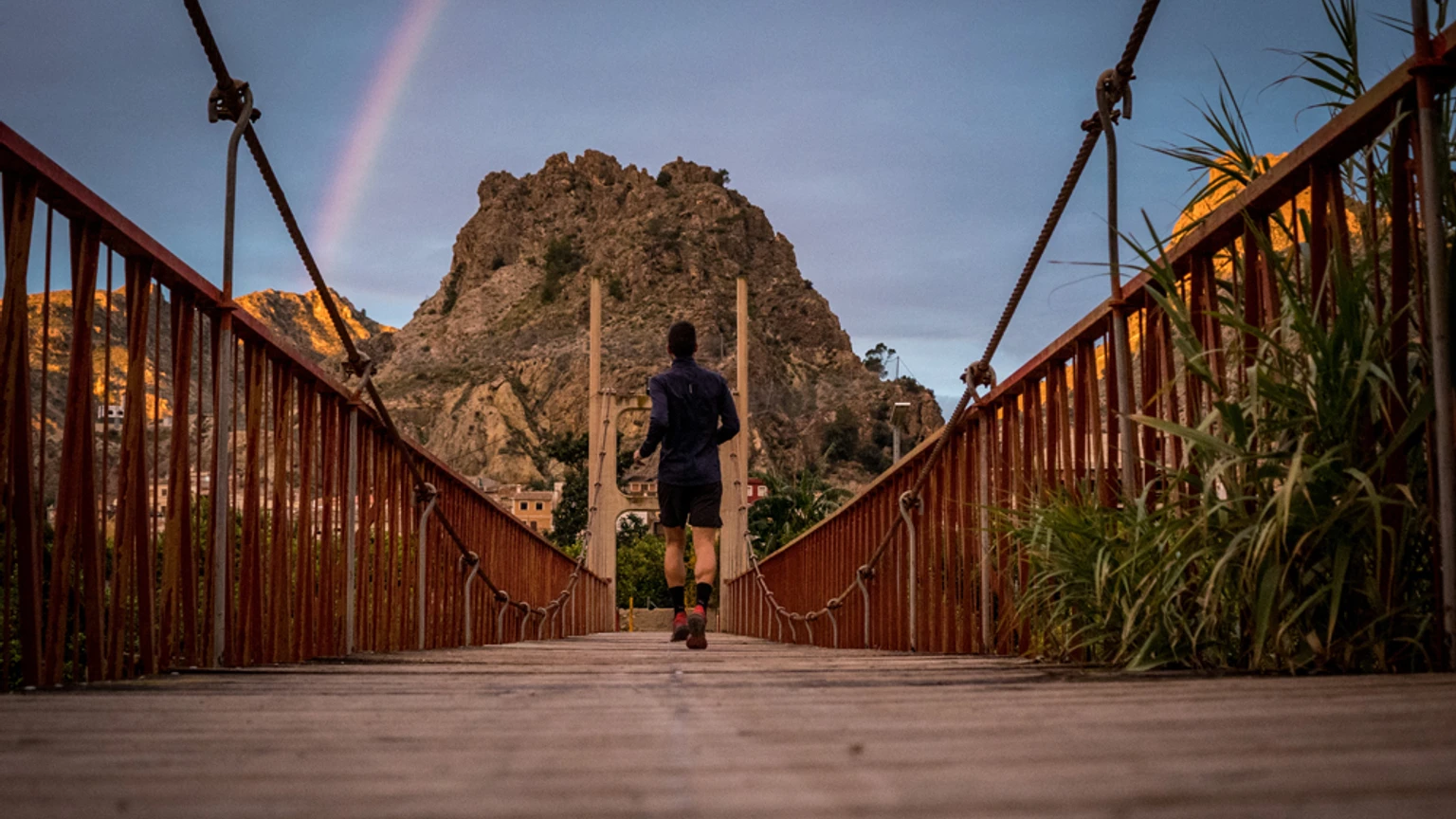 Corredor de trail sobre una pasarela en el entorno de Ojós, con la montaña al fondo.