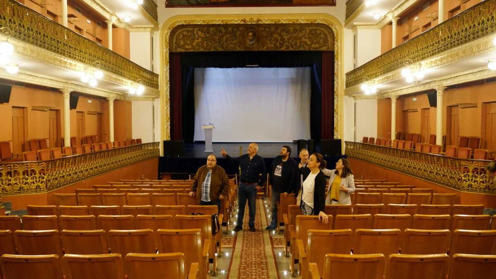 Patio de butacas, palcos dorados y escenario del Teatro Cervantes de Abarán con varias personas de pie en el pasillo central