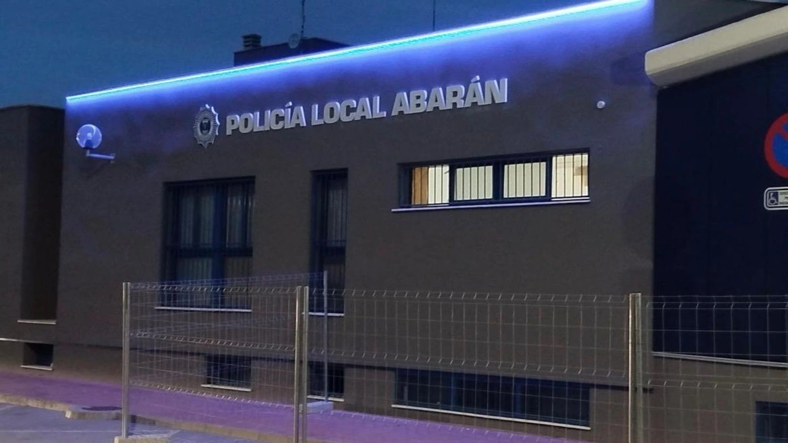 Fachada renovada de las dependencias de la Policía Local de Abarán al anochecer, con rótulo iluminado y vallas de obra en la acera.
