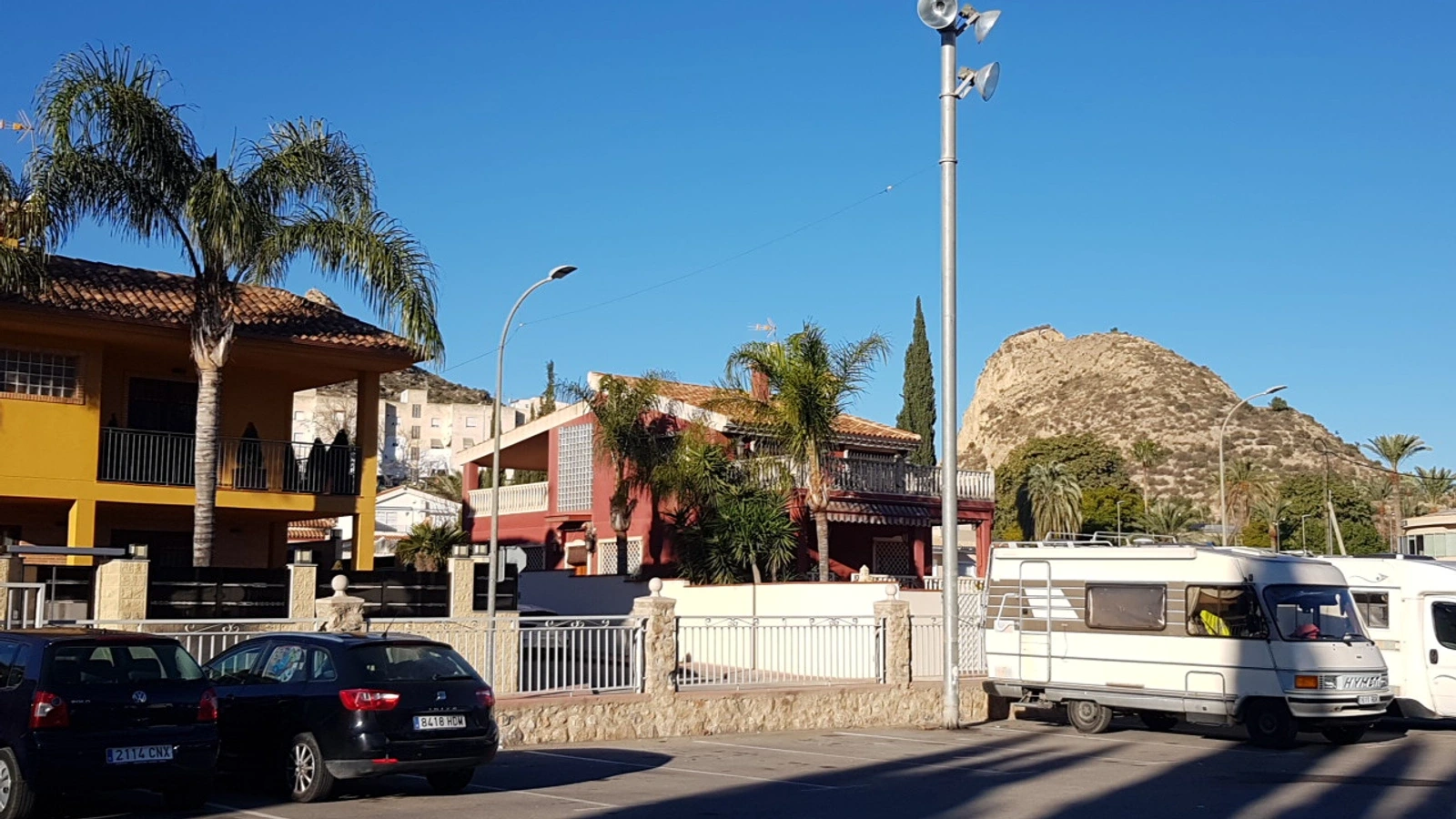 Viviendas unifamiliares y bloques de pisos en una calle de Archena, con el monte Ope al fondo y vehículos aparcados.