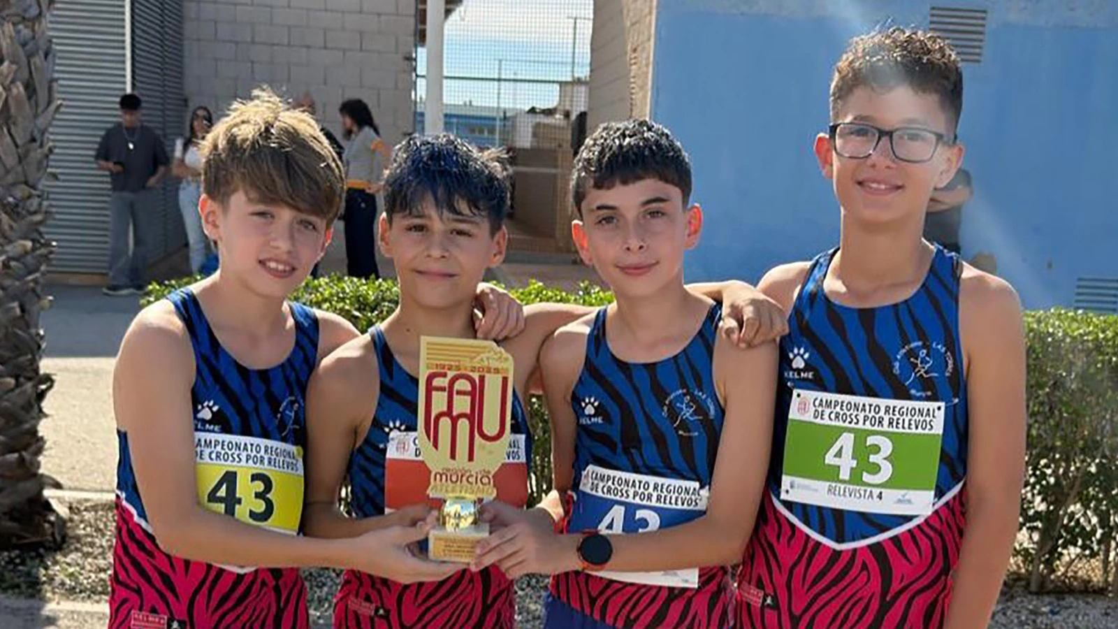 Cuatro atletas sub-14 del Atletismo Las Torres posan con el trofeo de campeones regionales de cross por relevos.