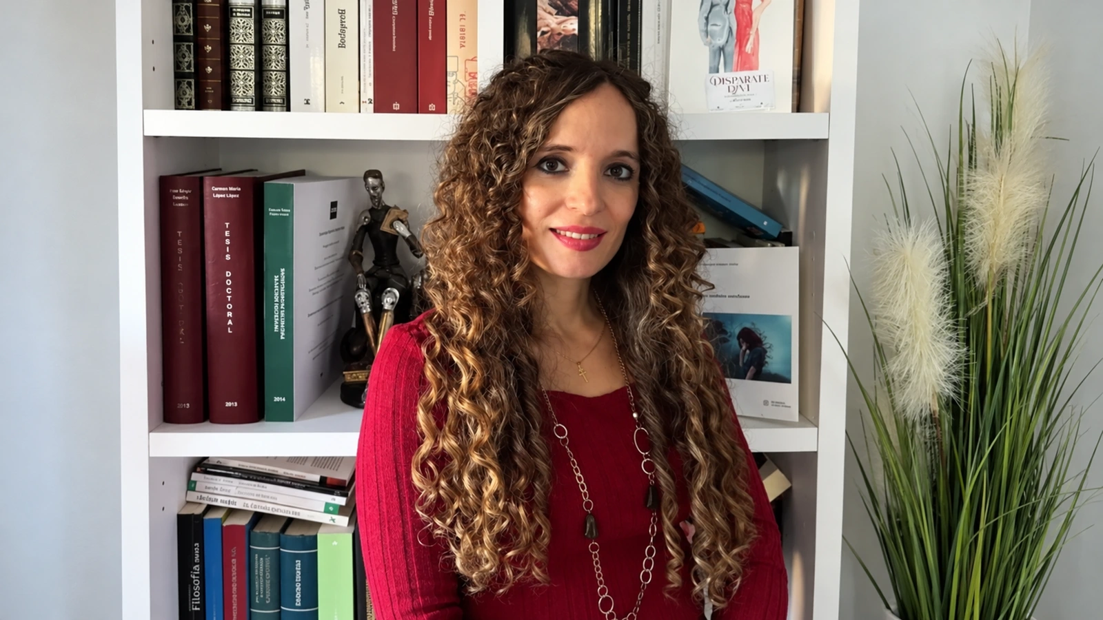 La escritora Carmen María López, con una blusa granate ante una estantería de libros