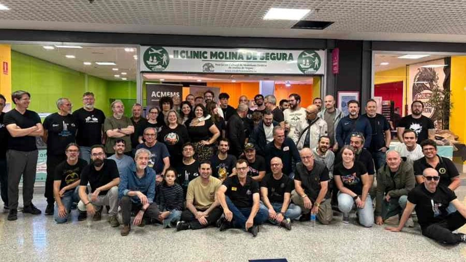Foto de grupo de participantes e instructores bajo el rótulo del II Clinic Molina de Segura de modelismo