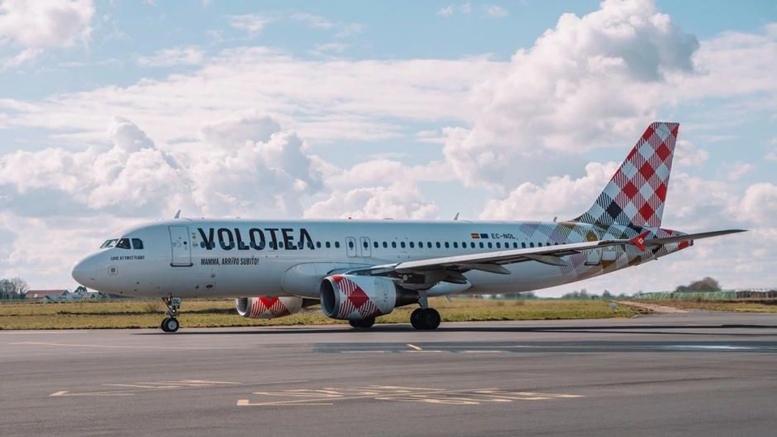 Avión Airbus de Volotea, con la cola de cuadros rojos y blancos, rodando por una pista bajo un cielo con nubes