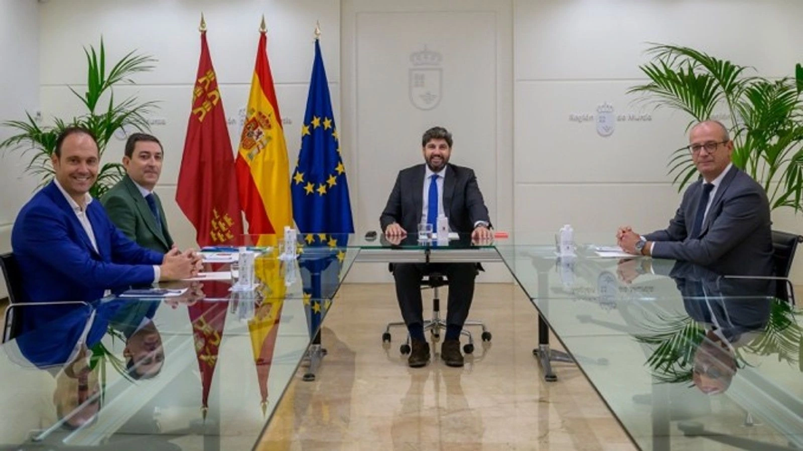 Reunión en una sala institucional del Gobierno regional con banderas de la Región de Murcia, España y la Unión Europea.