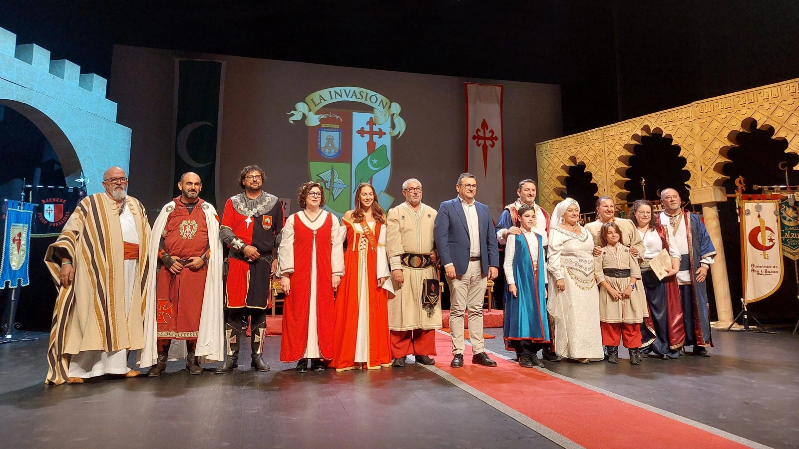 Festeros con trajes de moros y cristianos posan en el escenario del Teatro Capitol de Cieza ante el escudo de La Invasión