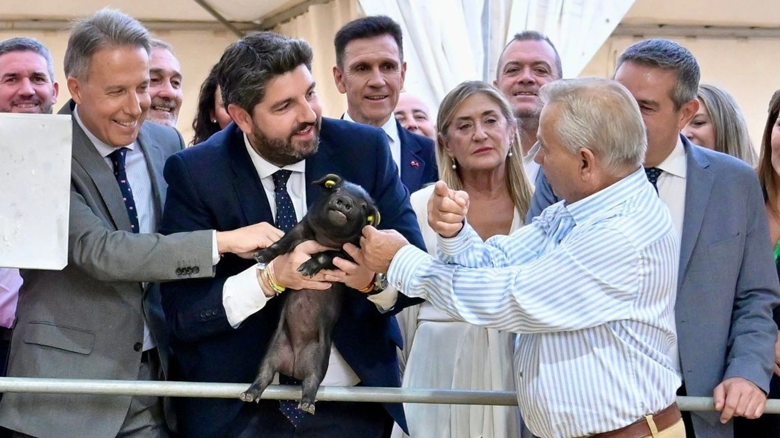 Fernando López Miras sostiene un lechón negro junto a un ganadero y otras autoridades en un recinto de la feria Sepor de Lorca