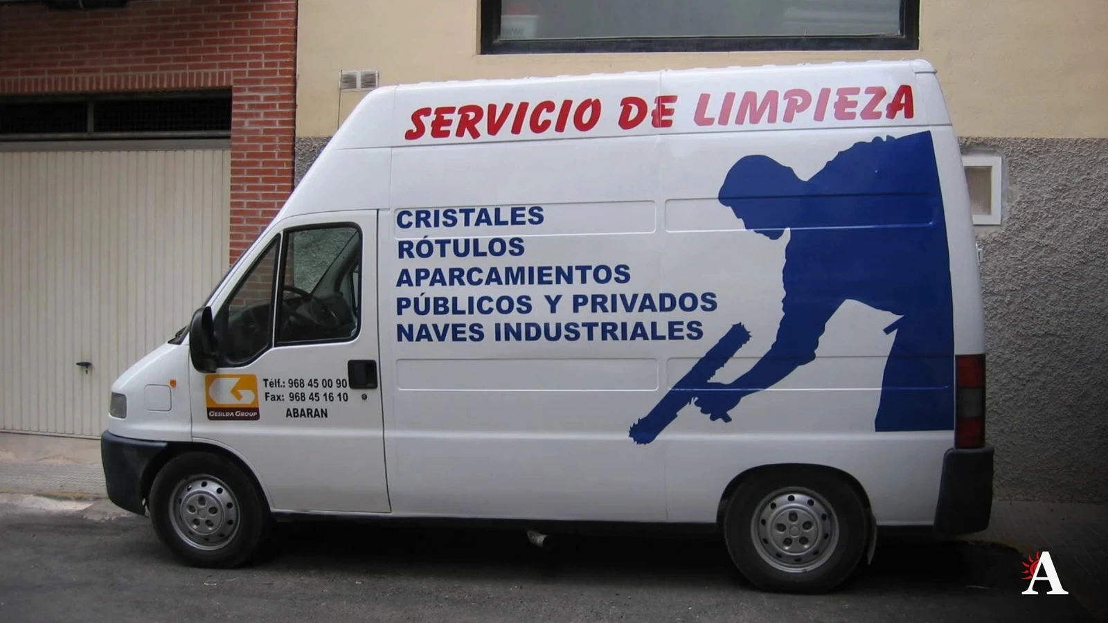 Furgoneta blanca rotulada con el texto Servicio de limpieza, cristales, rótulos y aparcamientos, aparcada junto a una fachada en Abarán