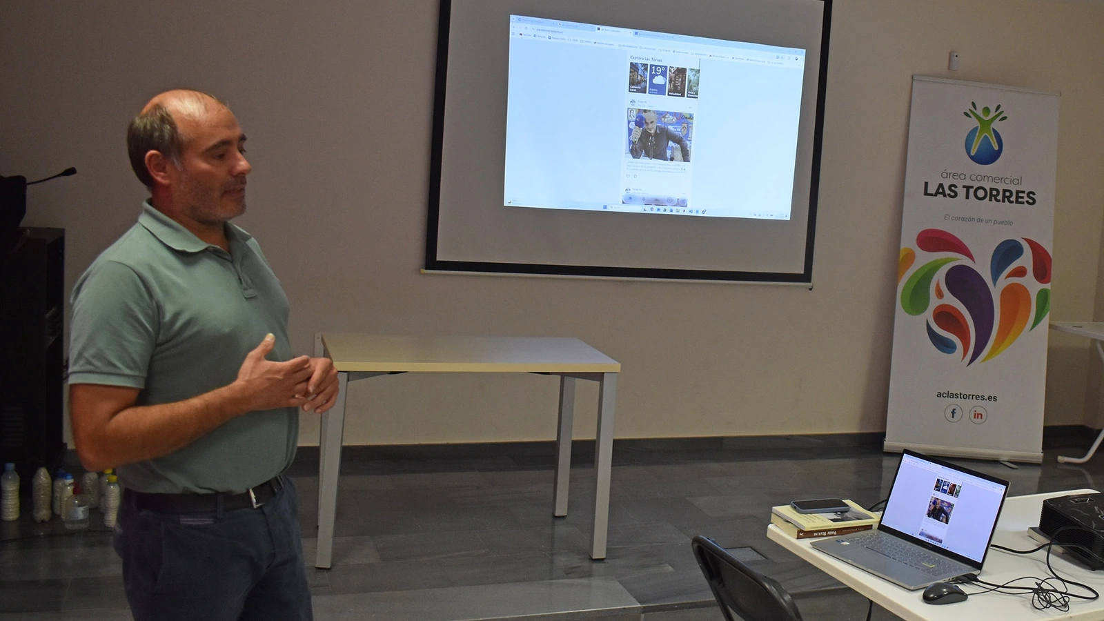 Antonio Vicente presenta la aplicación Las Torres Conectados ante una pantalla con la app proyectada y el cartel del Área Comercial Las Torres.