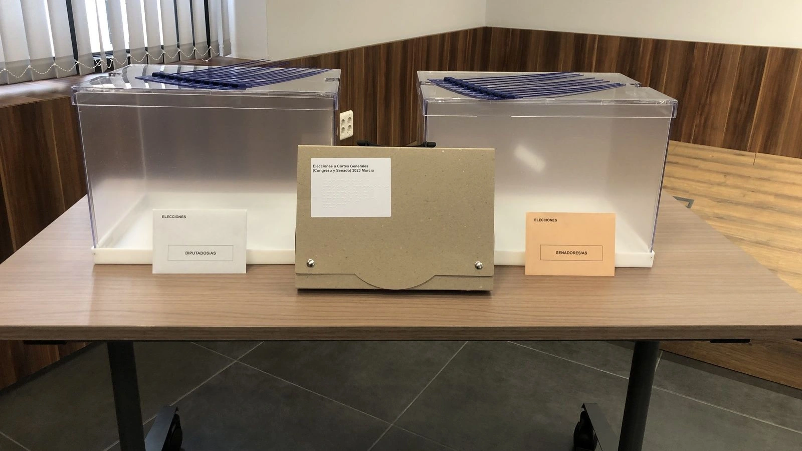 Dos urnas transparentes sobre una mesa con sobres para Diputados y Senadores y una caja de documentación electoral de Murcia.