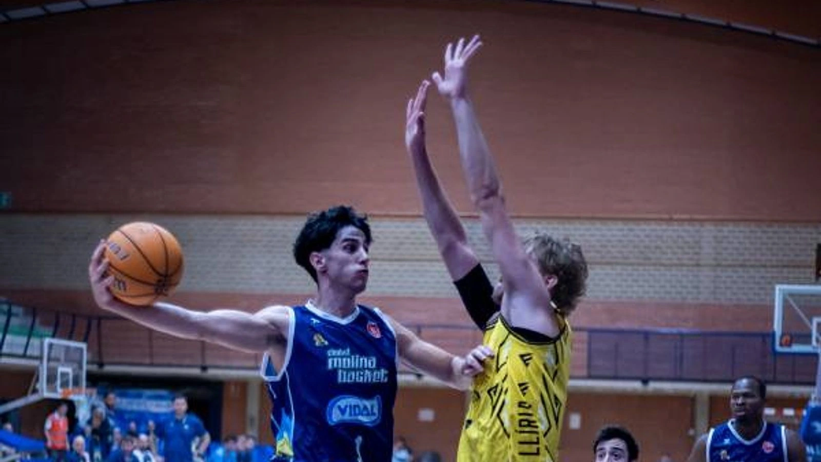 Un jugador del Ciudad Molina Basket, de azul, protege el balón ante un defensor del CEB Llíria, de amarillo, en el Pabellón Serrerías.