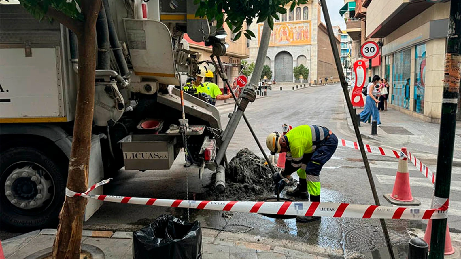 Operarios con casco y chaleco reflectante trabajan junto a un camión en una calle de Murcia acotada con cinta
