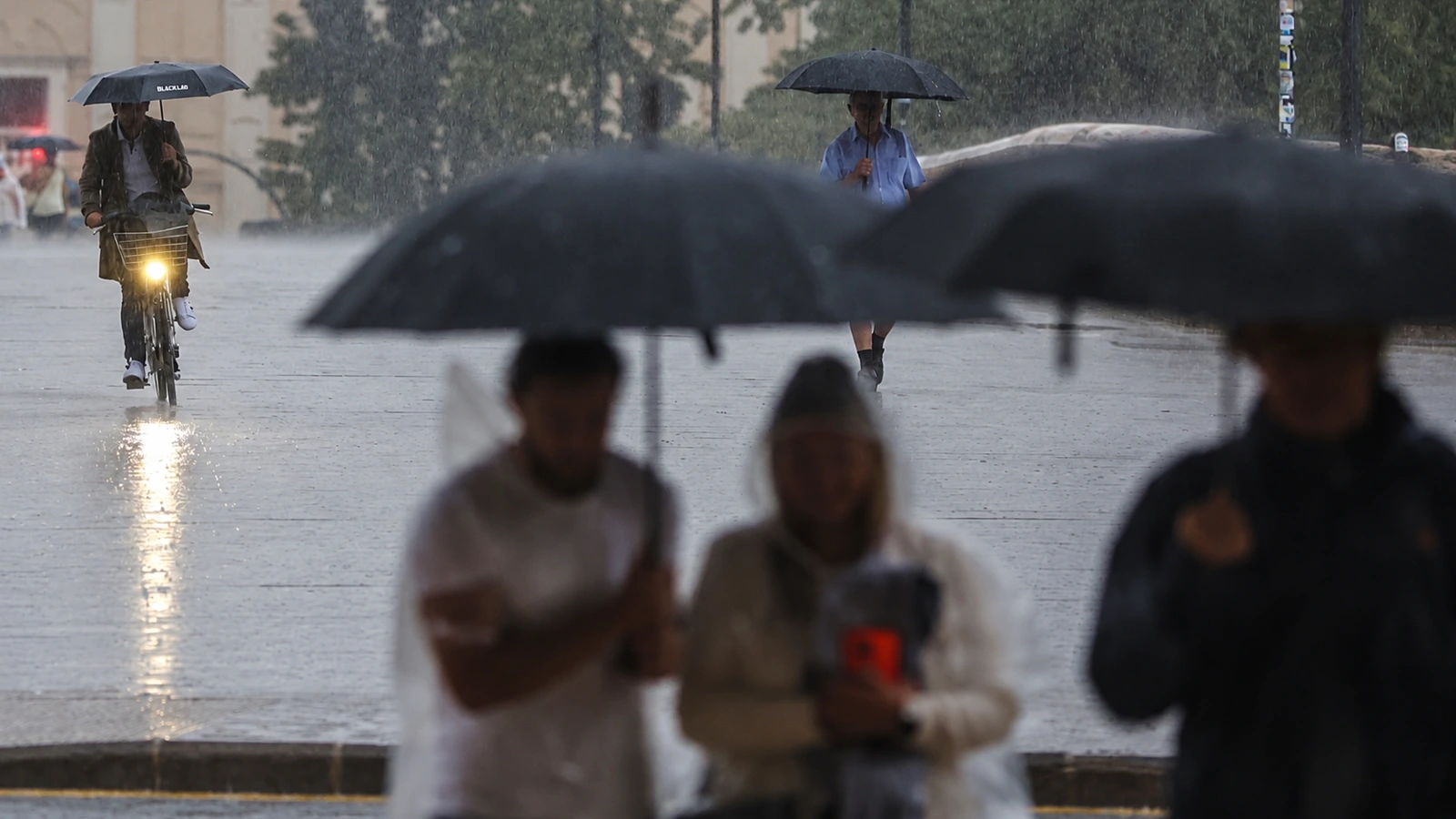 Peatones con paraguas y un ciclista bajo la lluvia en una fotografía de archivo