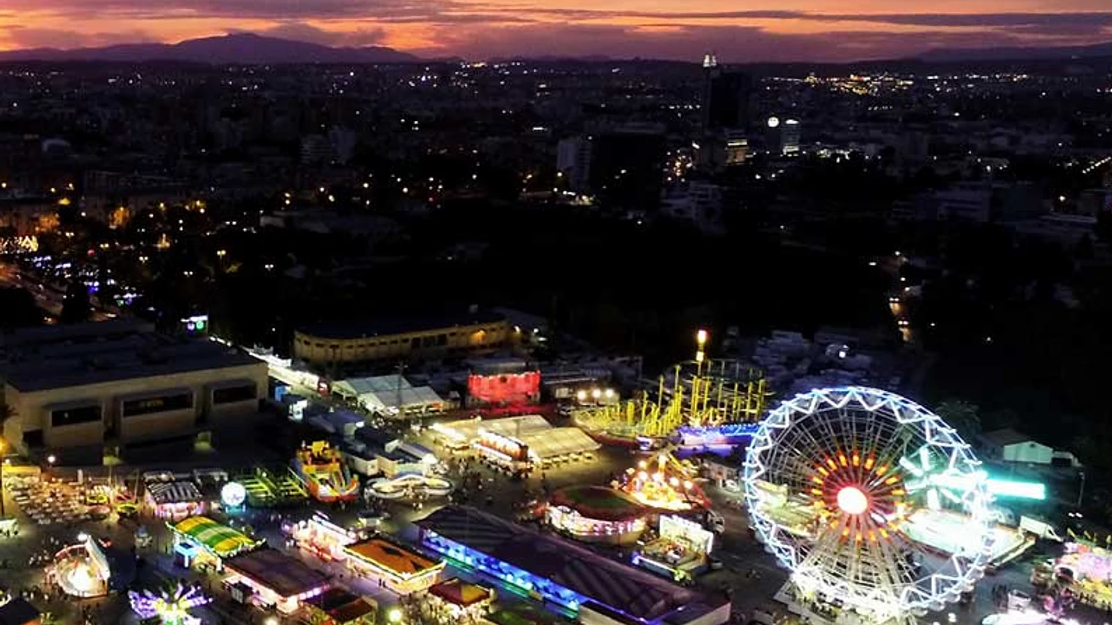 Vista nocturna de la Feria de Murcia con atracciones iluminadas y una noria sobre la ciudad