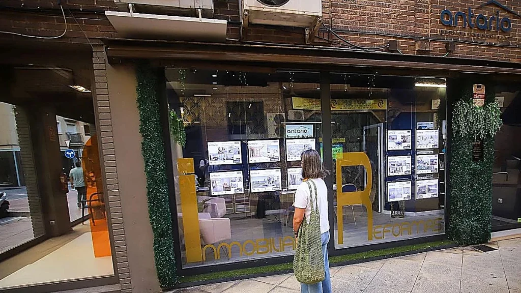 Mujer consulta anuncios de viviendas en el escaparate de una inmobiliaria de la Región de 