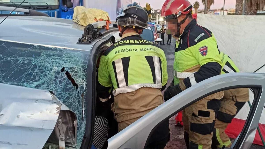 Bomberos del CEIS trabajan junto al turismo siniestrado tras chocar con un camión en la N-344