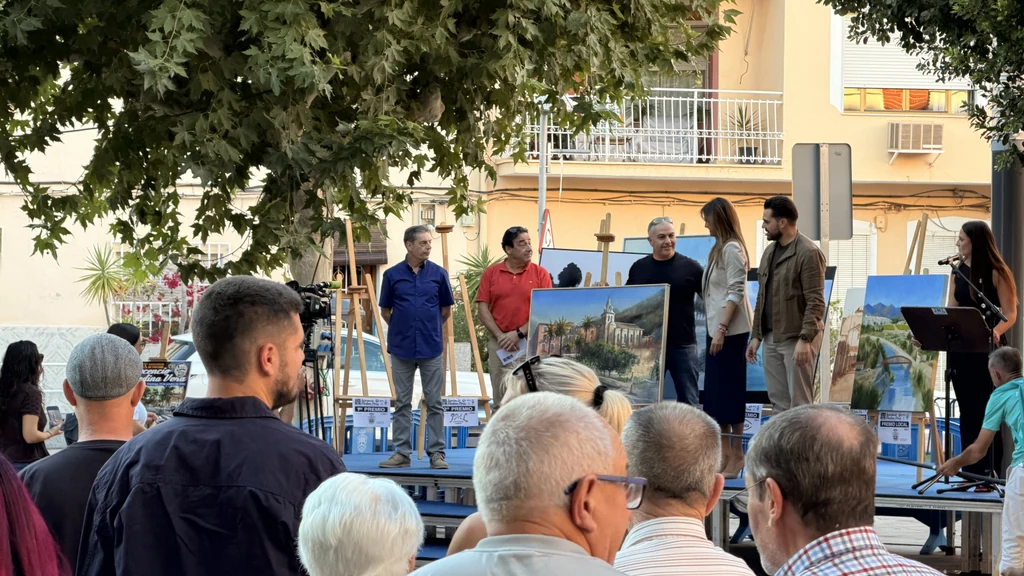 Obras del XIX Concurso de Pintura Inocencio Medina Vera expuestas en caballetes sobre el escenario de la plaza Primero de Mayo de Archena durante la entrega de premios