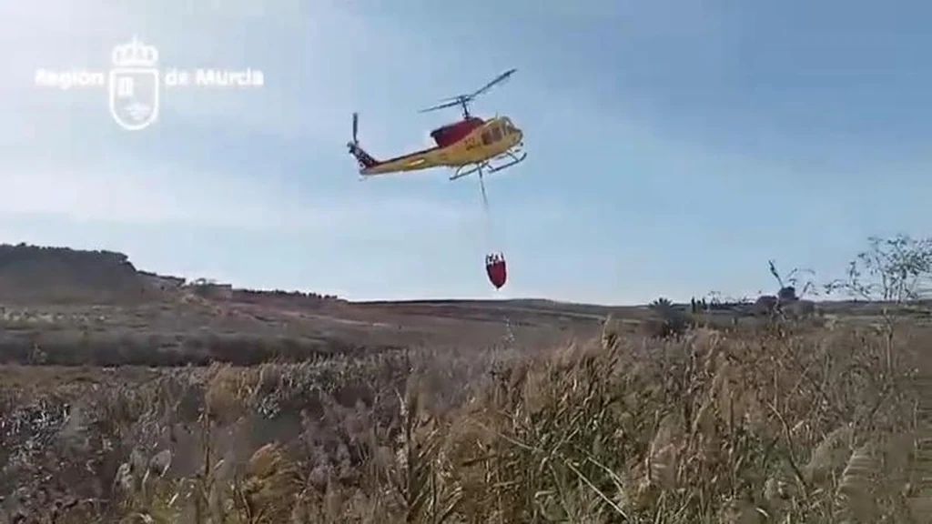 Helicóptero de emergencias con helibalde sobre el carrizal incendiado en Villanueva del Río Segura